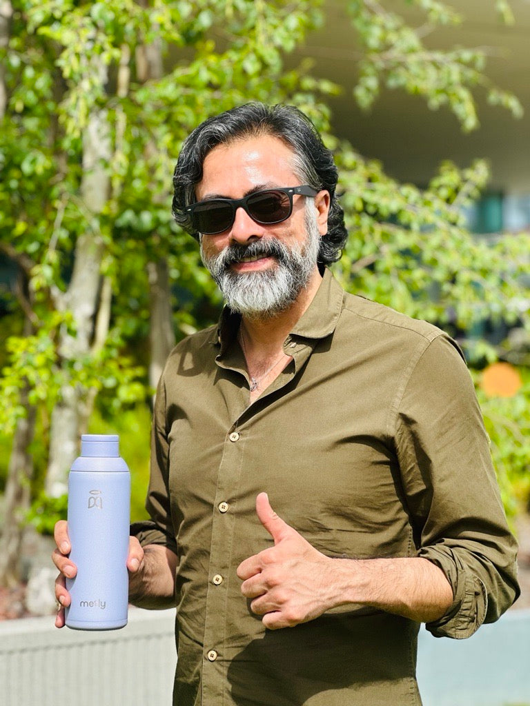 Man with sunglasses holding a Metly Periwinkle 500ml filtered water bottle and giving a thumbs up outdoors