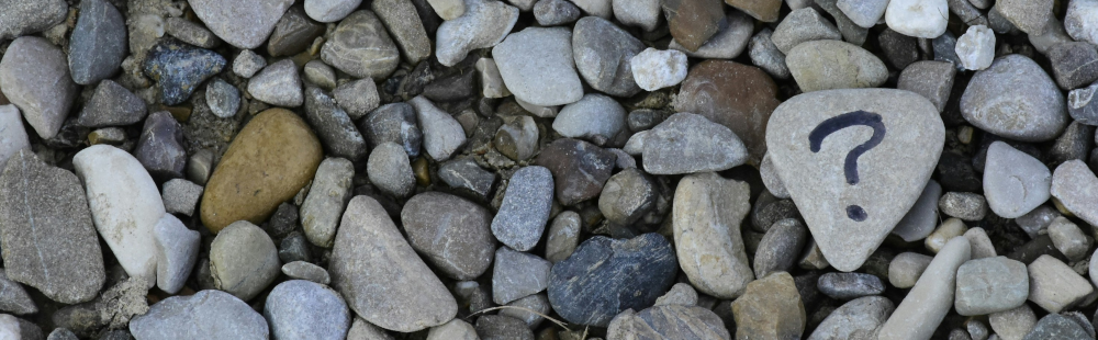 Assortment of pebbles on ground with a question mark drawn in black pen