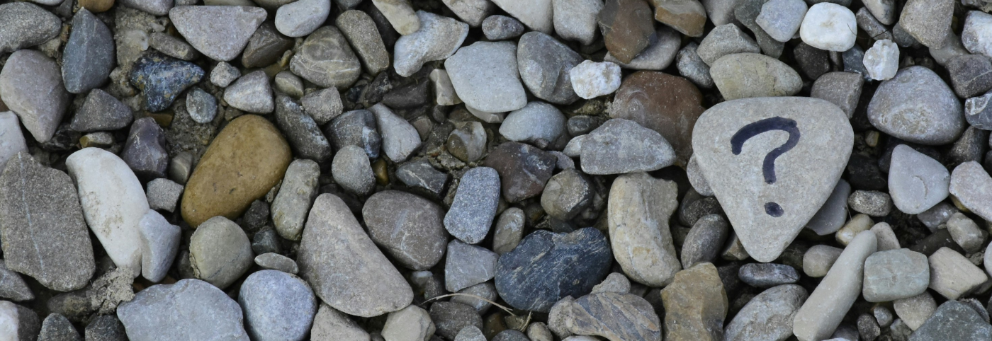 An assortment of pebbles of different sizes featuring a larger pebble with a question mark drawn in black marker pen